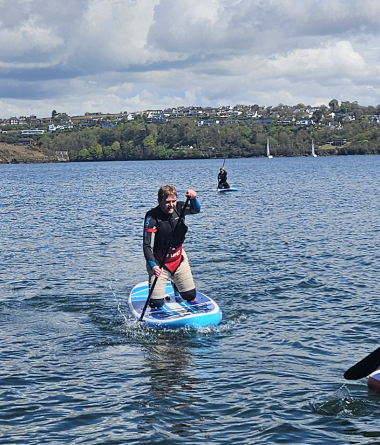 Person balancing on a paddleboard in open water under a partly cloudy sky